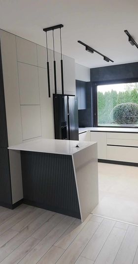 Biała matowa kuchnia z półwyspem, czarnymi akcentami, lamelowym bokiem i dużym oknem.